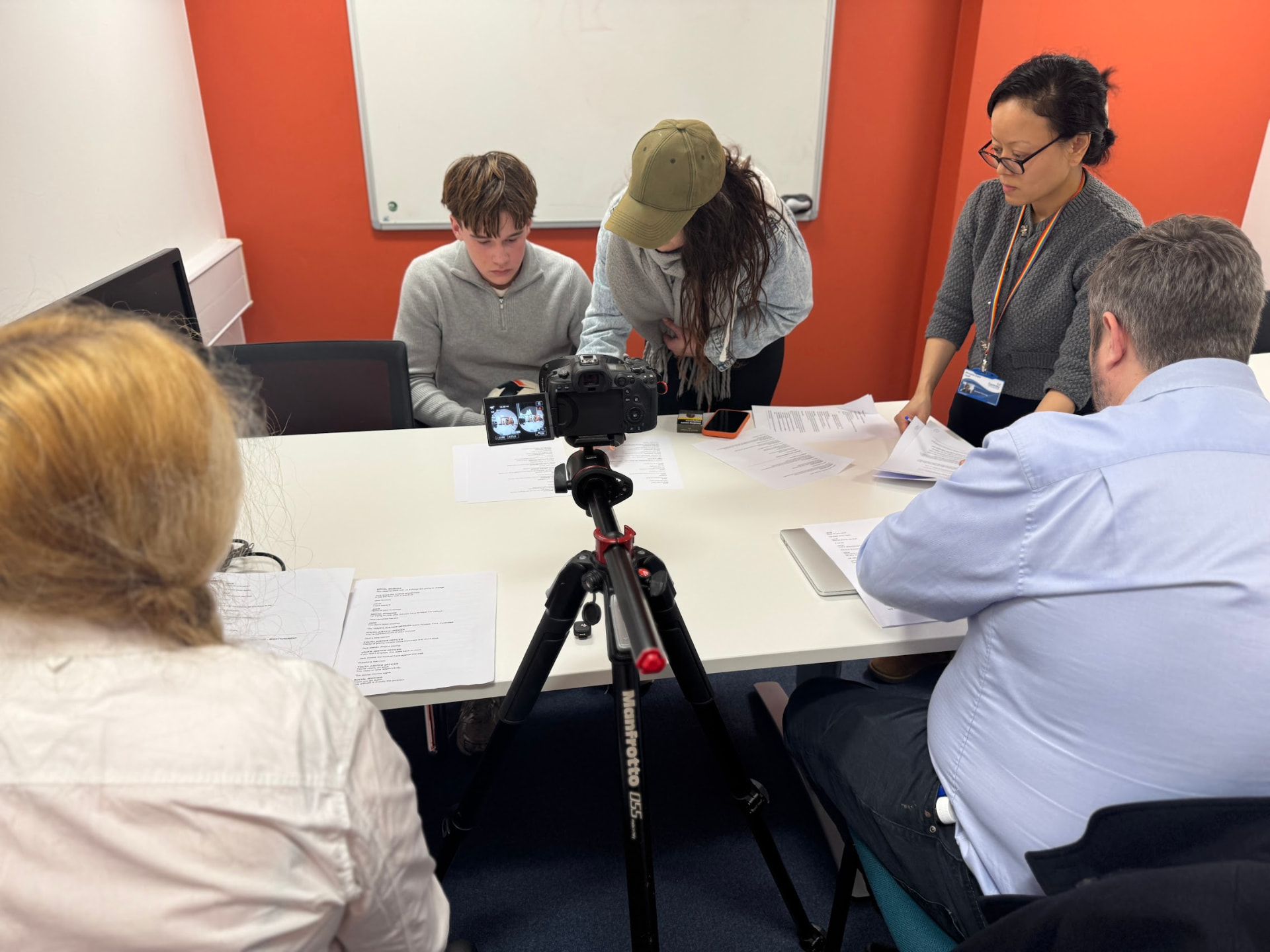 The production team on set around a table with scripts, filming with the camera on a tripod
