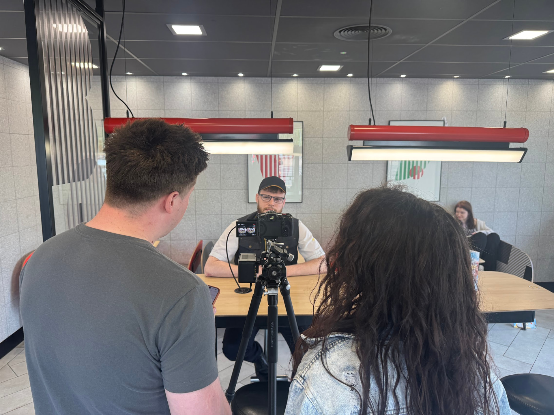 Crew filming a McDonald's crew member seated at a table under the restaurant lights