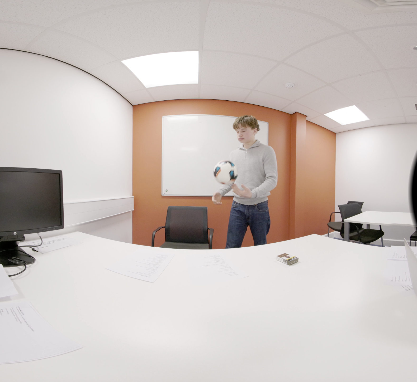 Still from the 3D 180° film: the same teenager waiting alone in a meeting room, spinning a football